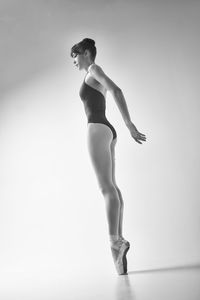 A ballerina in a bodysuit and pointesposes in a photo studio in motion showing beautiful long legs