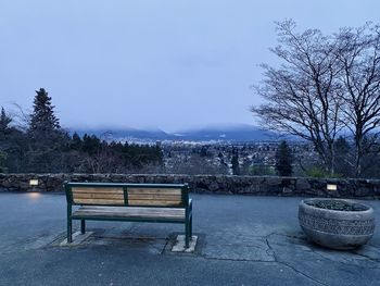 Empty bench in park against sky
