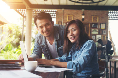 Portrait of happy male and female freelancers working on laptop at cafe