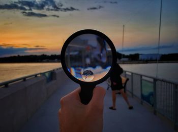 Close-up of hand holding magnifying glass against sky