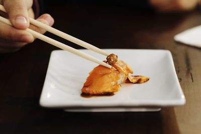 Hand of a man using chopsticks to hold a piece of nigiri sushi. 
