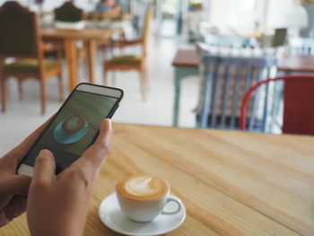 Close-up of hand holding coffee cup on table