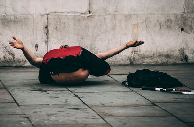 Man sitting on footpath against wall