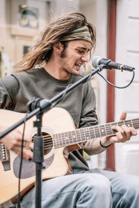 Young rocker with long hair and a headband playing guitar in front of a microphone