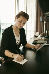 Businesswoman with digital tablet writing on note pad in hotel room