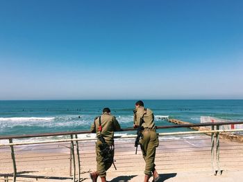 Rear view of security guards with guns standing by railing at beach