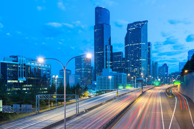 Light trails on road amidst buildings against sky at night