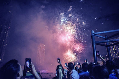 Crowd photographing firework display through mobile phone at night