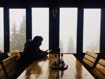 Side view of silhouette man using phone while sitting at restaurant table