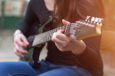 Midsection of woman playing guitar outdoors