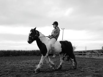 Girl riding horse on field against sky