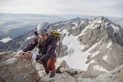 Female rock climber wearing helmet climbs a cliff in the tetons