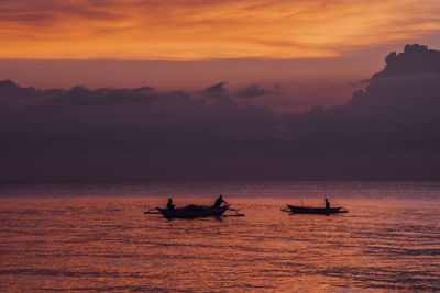 Silhouette people rowing boats in sea against mountains during sunset