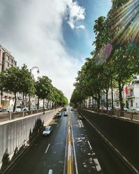 Cars on road amidst trees against sky in city