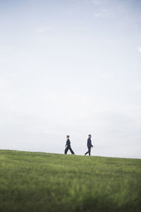 Side view of friends walking on grassy field against cloudy sky