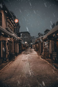 Illuminated street amidst buildings against sky during rainy season