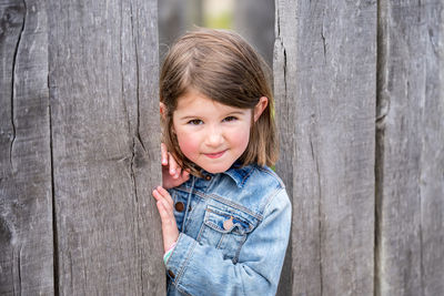 Portrait of smiling girl standing by plank outdoors