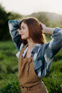 Woman with hands behind head standing on field