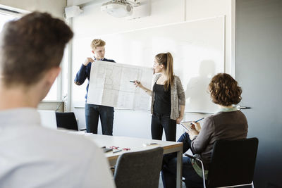 Young woman showing flipchart to friends and professor in classroom