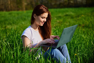 Young woman using laptop while sitting on field