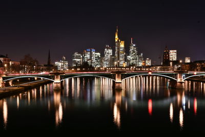 Illuminated bridge over river with buildings in background at night