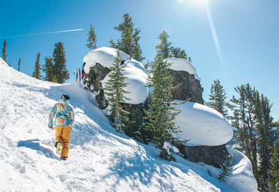 Rear view of hiker climbing on snow covered rocky mountain against sky during sunny day