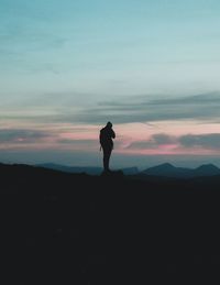 Silhouette woman standing on landscape against sky during sunset