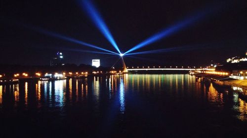 Illuminated buildings by river against sky at night