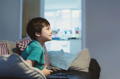 Boy looking away while sitting on bed at home