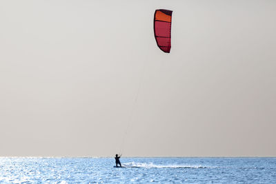 Person paragliding in sea against sky