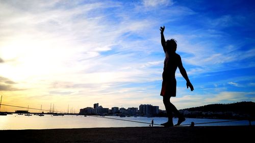 Silhouette woman with arms raised against sky during sunset