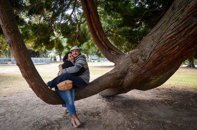 Full length of couple embracing while sitting on tree