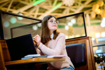 Young woman using mobile phone while sitting on laptop