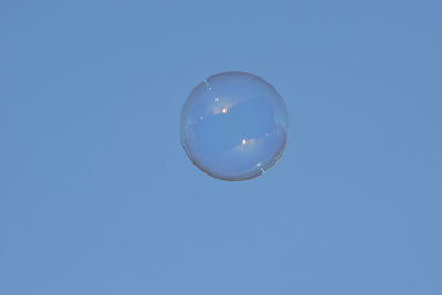 Low angle view of bubbles against clear blue sky