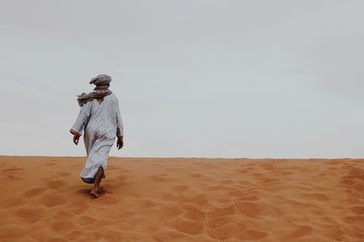 Rear view of man walking on sand dune