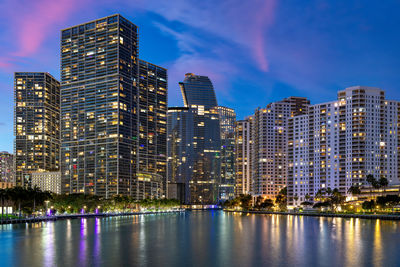 Illuminated buildings by river against sky at night