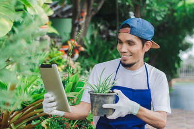 Smiling botanist holding digital tablet with potted plant