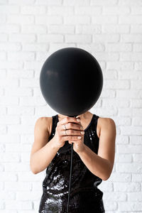 Woman holding balloon standing against wall at home