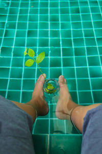 Low section of person holding glass in swimming pool