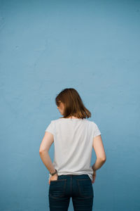 Rear view of young woman standing against blue wall