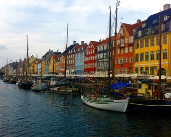 Sailboats moored on river by buildings against sky