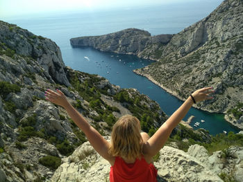 Rear view of woman with arms raised sitting on cliff