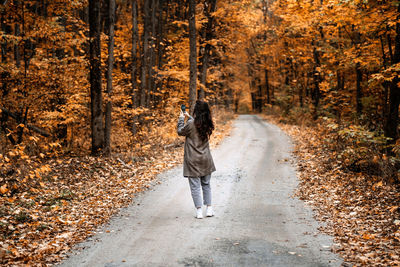 Woman taking pictures in autumn forest. mobile photography, film photography, taking photos