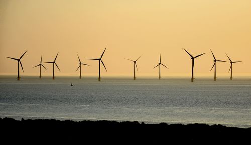 Wind turbines on beach against sky during sunset