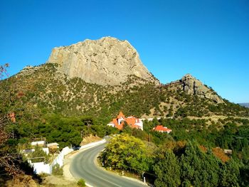 Empty country road by mountains against clear blue sky