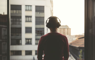 Man wearing headphones on a balcony in the city at sunset