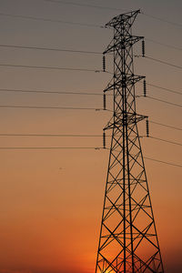 Low angle view of silhouette electricity pylon against sky at sunset