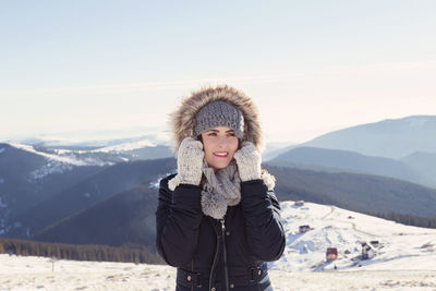 Cheerful woman wearing fur coat while standing against mountains during winter