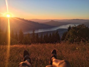 Low section of man on mountain against sky during sunset