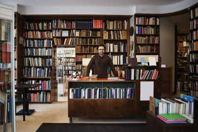 Portrait of owner standing against bookshelves in library